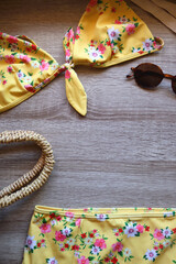 Floral yellow bikini, wicker bag, retro sunglasses, seashell, bag with peaches and cut watermelon on wooden background. Top view, copy space.