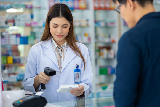 Asian female pharmacist holding bar code reader scanning pills box at the pharmacy. Shelves with drug and Health Care product