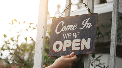 Woman setting open sign board through the door glass., Owner of a small business changing the sign for the reopening.