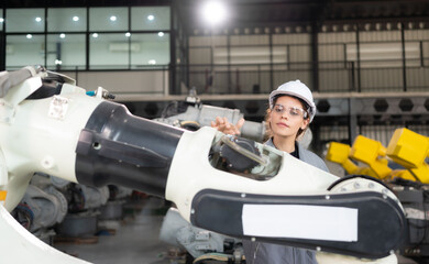 A female engineer installs a program on a robotics arm in a robot warehouse. And test the operation before sending the machine to the customer.