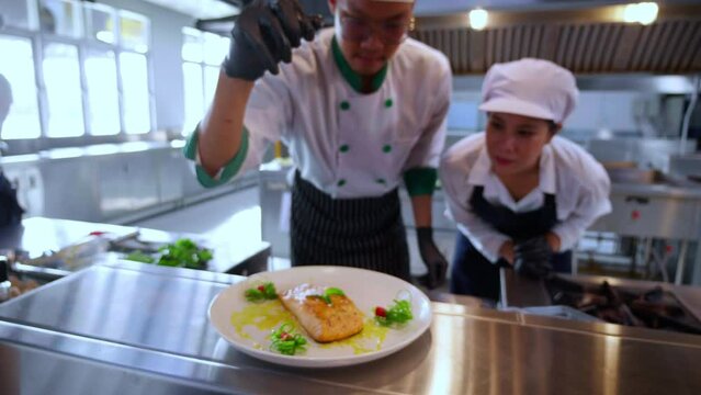 Closeup hands of chef man cooking salmon steak and decoration on plate with professional in kitchen at restaurant, food and garnish for serving, food japan, culinary and recipe with delicious.