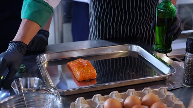 Closeup hands of chef preparing marinated slice salmon fish raw for cooking food while put ingredient and condiment at kitchen, meat and recipe for delicious, gastronomy seafood and nutrition.