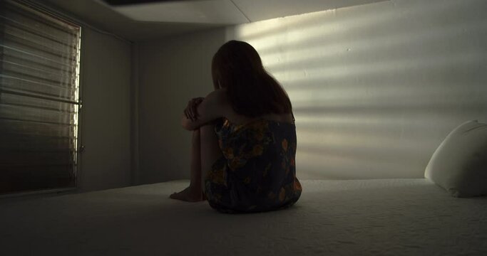A lonely woman is sitting on the bed in a narrow dark room. This concept use for symptoms of stress, major depressive disorder (MDD), psychotic symptoms.