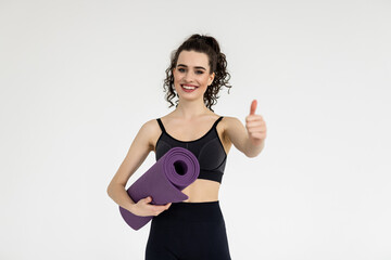 Young sport woman going to yoga classes while holding a mat isolated on white background with thumbs up