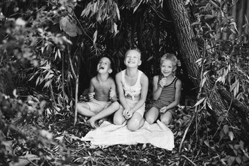 Three village children are playing in a hut which they themselves have built from leaves and twigs. Wooden house in the forest. Black and white photography