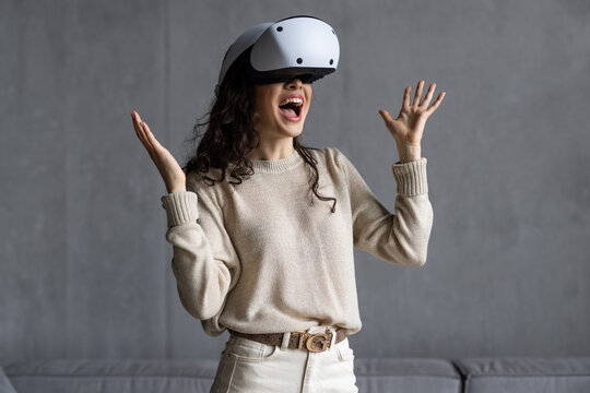 Beautiful young girl in virtual reality headset. Augmented Reality. Happy woman holds 3D vr glasses indoors, wide smiles opens mouth in happy expression.
