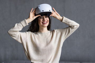 Attractive young woman adjusting her VR headset and smiling while sitting on the carpet at home