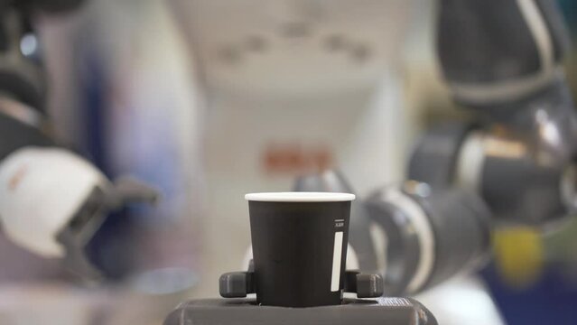 Motion of robotic arm making coffee. Robotic arm takes paper coffee cups. Mechanical robotic arm gives cup of coffee to a customer.