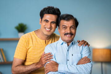 Happy smiling adult son standing by holding senior father by looking camera at home - conept of...