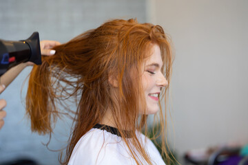 Naklejka premium Portrait happy female customer at the hair salon. Professional hairdresser blow drying with hairdeyer to female customer in hair salon.