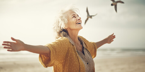 Happy senior woman standing on the beach with open arms, enjoying summer and freedom