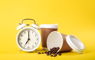 Alarm clock, paper cup and coffee beans on a yellow background isolated.