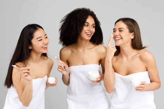 Beauty and skincare concept. Three diverse women with different types of skin applying face cream over grey background