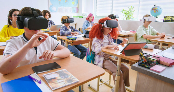 Smart pupils wearing VR headsets and studying with future technologies at classroom. Excited boys and girls in virtual glasses experienced augmented reality at lesson in school.