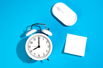 White alarm clock and blank white paper sticker on a blue background isolated.