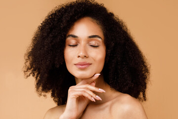 Sensual young black lady touching her face with closed eyes, enjoying silky smooth skin after face care routine