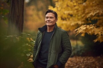Portrait of mature man standing in autumnal park, smiling.