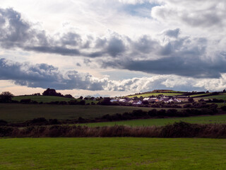 clouds over a small Irish village on a summer evening. Irish settlement in County Cork, dramatic landscape. European countryside, rustic landscape. Green grass field under cloudy sky