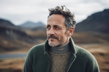 Portrait of a handsome middle-aged man in a green sweater on the background of the mountains.