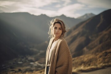 Fototapeta premium Young woman with long blond hair in beige sweater on the background of mountains