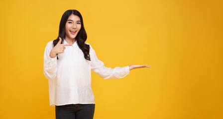 Happy young Asian teen woman standing with her finger pointing presenting isolated on yellow...