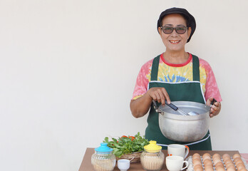 Happy Asian senior woman is cooking, wear chef cap and apron, holds pot and ladle. Concept, Cooking...