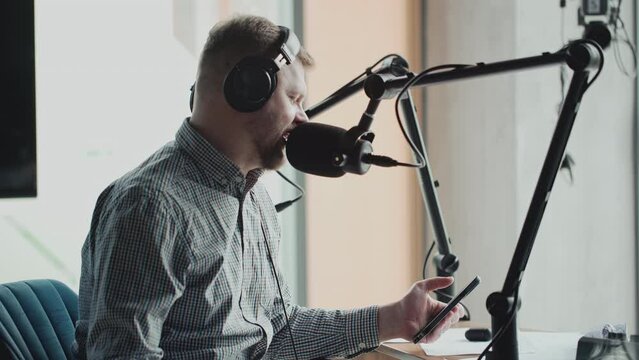 Handsome smiling radio host working in studio with microphone and headphones.