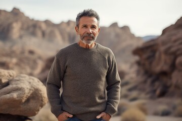Full-length portrait photography of a cheerful man in his 50s wearing a cozy sweater against a rock formation or cliff background. Generative AI