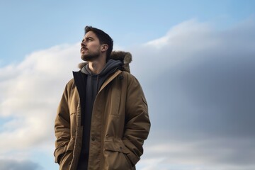 Handsome young man in coat looking away while standing against cloudy sky