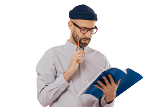 Concentrated unshaven adult man holds blue textbook and pencil, reads necessary information, has serious facial expression, wears formal clothes, isolated over pink background. Copywriter indoor