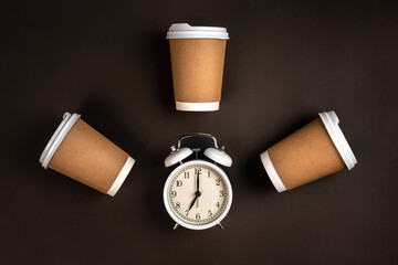 White alarm clock and craft disposable cups on a dark background, top view.