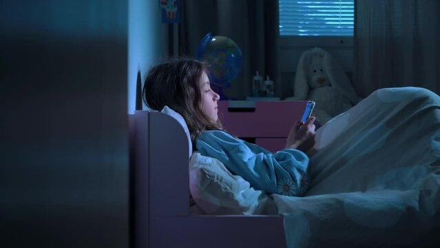 Teen girl lying in bed at night using smartphone, scrolling social media and texting. Not healthy sleep. Insomnia and the harm of the smartphone before going to bed. Dependence on social networks