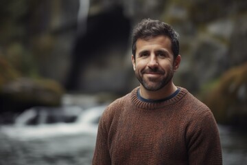 Portrait of a smiling handsome man in a sweater standing in front of a waterfall