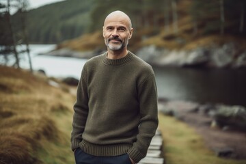 Handsome middle-aged man in a green sweater standing by the lake.