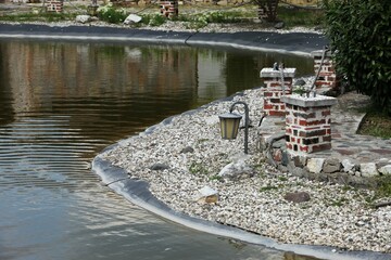 Fototapeta na wymiar pebble bank next to a small pond, lantern on the bank and brick pillars