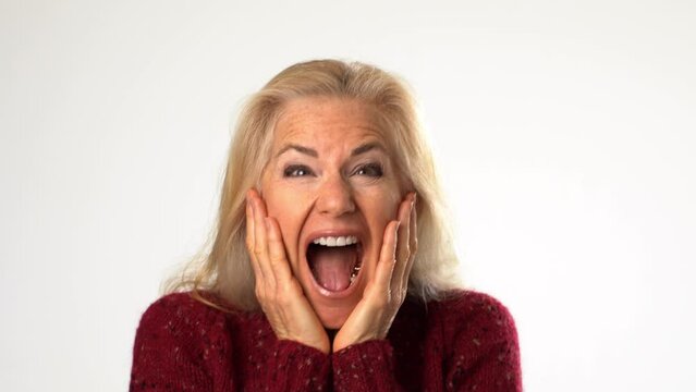 Closeup of excited shocked surprised middle age mature blonde woman lady 50s years old says wow omg no way say yes celebrating put hands on face isolated solid white background studio portrait