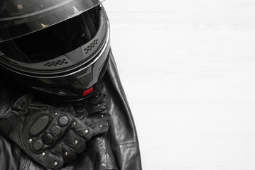 A motorcycle helmet, leather jacket and sport gloves on the white wooden table background with copy space.