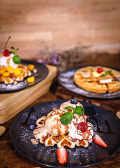 Delicious homemade waffles with fresh fruits, ice cream, meringue, strawberry, marshmallow, blueberry, mango, colorful candy, different toppings, banana, jam - sweet food