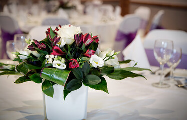 Table arrangment of white and red flowers with green leaves for a wedding ceremony