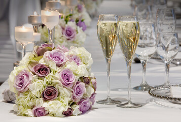 Beautiful bridal bouquet of dusky pink roses with white hydrengas with two crystal flutes of champage on wedding celebration table