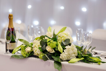 Beautiful arrangement of white rose and hydrangea and green viburnum and lily with champagne and glasses for the top table at wedding ceremony