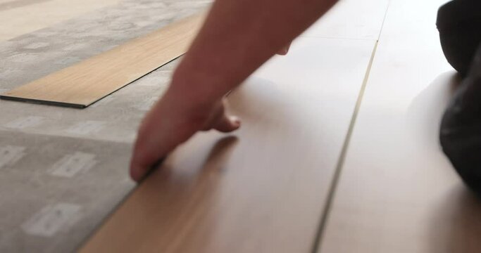 Man kneeling and installing wood laminate floor in a home. Closeup on male hands.