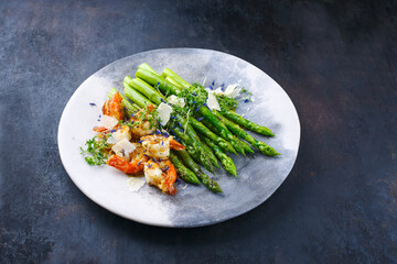 Green asparagus glazed with fried king prawns and parmesan cheese served as close-up on a design plate with text space
