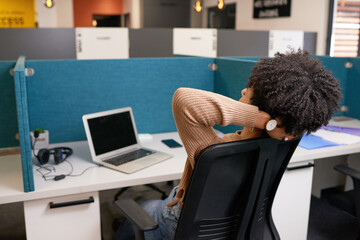 Young multi-ethnic woman leans with arms behind head, taking break in office