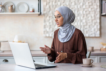 Online psychotherapy session. A young female Muslim psychologist in a hijab sits at home in front of a laptop and conducts a remote therapy consultation with a patient. - obrazy, fototapety, plakaty