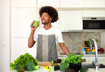 Happy Black Guy Drinking Glass Of Green Smoothie In Kitchen