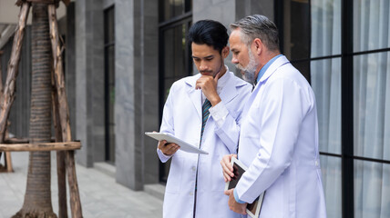 senior caucasian doctor and young intern doctor having discussion about patient diagnosis on digital tablet computer at hospital outdoor - obrazy, fototapety, plakaty
