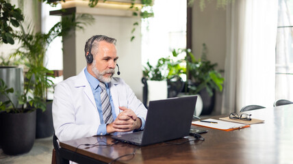 Fototapeta na wymiar Senior caucasian doctor online video call conference consult patient with headset on laptop computer. Doctor online consultation and telehealth medicine