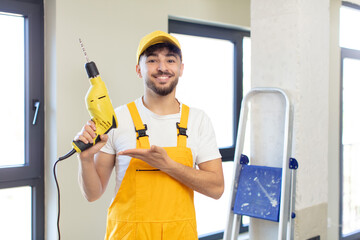young handsome man smiling cheerfully, feeling happy and showing a concept. handyman and drill...