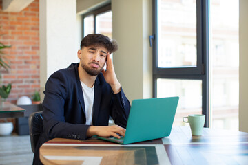 young handsome man feeling sad and whiney with an unhappy look and crying. freelance concept with laptop